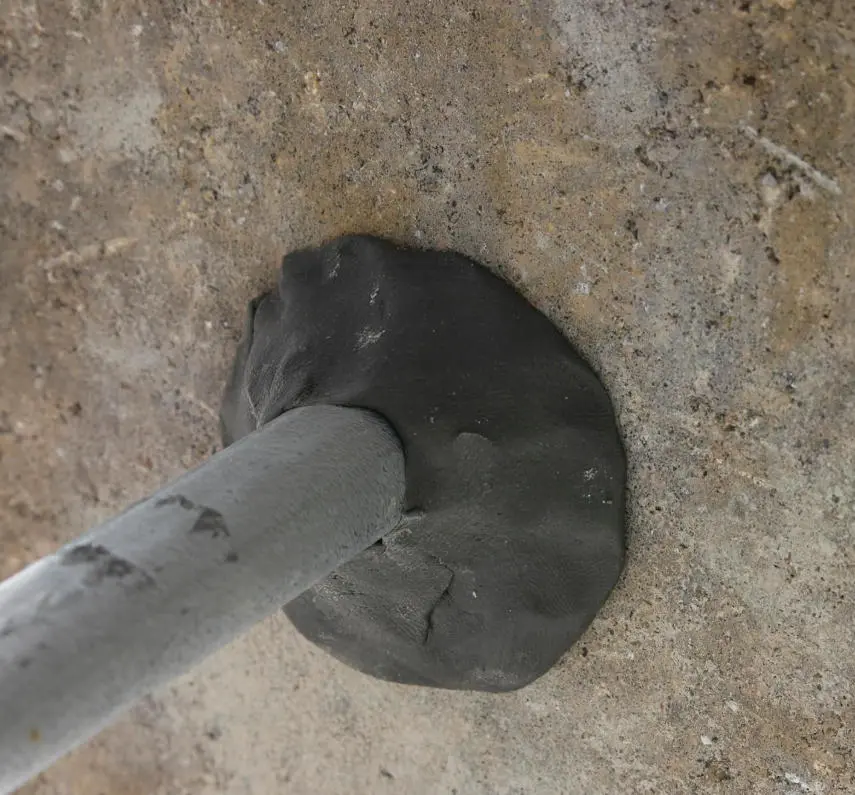 Black duct seal putty applied around pipe penetration in concrete wall to seal conduit entry